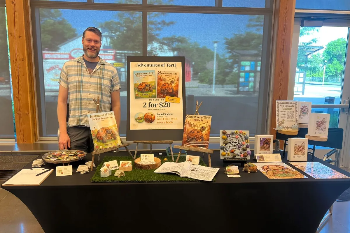 J.J. Hyatt standing behind the Adventures of Tertl vendor table at a Cold Blooded Expos show, with both books on easels, stickers, puzzles, and coloring pages on display